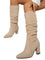 Bottes hautes en daim beige portées par une femme assise, présentées en gros plan dans un intérieur moderne. Le modèle possède un talon épais, une tige légèrement plissée et une finition élégante qui met en valeur un style contemporain et raffiné.