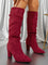 Bottes hautes en daim rouge portées par une femme debout, présentées en gros plan dans un décor intérieur élégant. Le modèle comporte un talon épais, une tige légèrement plissée et une finition moderne qui apporte une touche chic et audacieuse.