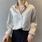 Une femme porte une chemise satinée beige avec un col classique. Les manches sont retroussées et la chemise est légèrement boutonnée, accompagnée d'un pantalon noir à taille haute. Elle porte également un collier délicat en or et tient un sac marron dans ses mains, ajoutant une touche chic à son ensemble.
